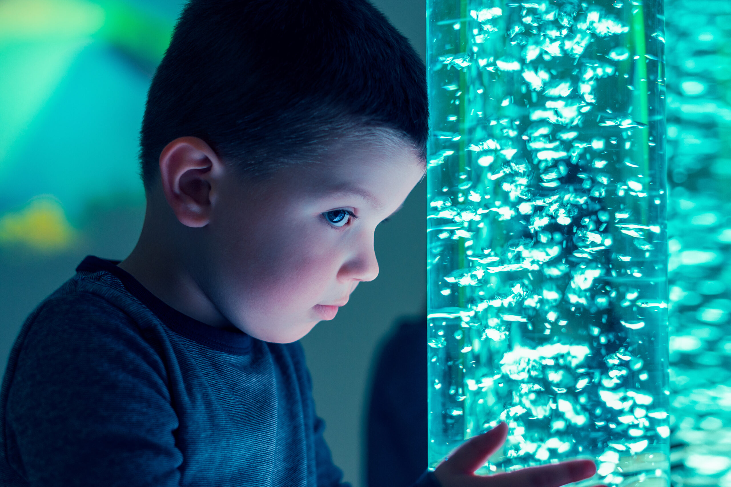 Child interacting with coloured lights bubble tube lamp during therapy session.